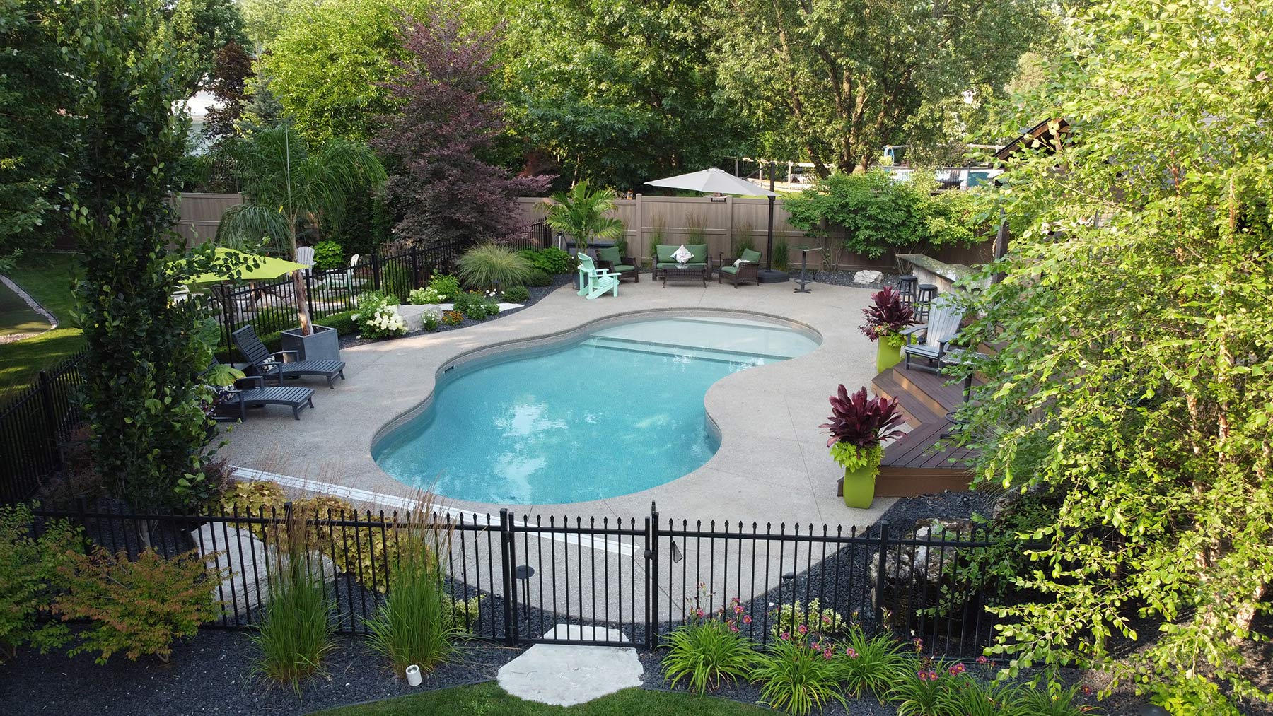 Gated pool surrounded by large shrubbery and greenery.